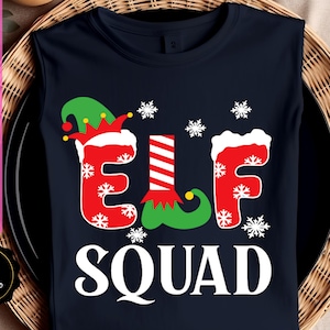 May include: Navy blue t-shirt with the words "ELF SQUAD" in a festive design. The word "ELF" is in red with white snowflake accents and a green elf shoe. The t-shirt is sleeveless.