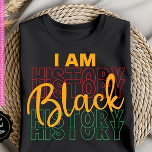 May include: Black t-shirt with the text "I AM HISTORY BLACK HISTORY" in red, yellow, and green.