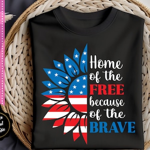 May include: A black t-shirt with a red, white, and blue sunflower design. The sunflower is made up of the American flag. The text "Home of the FREE because of the BRAVE" is printed on the shirt.