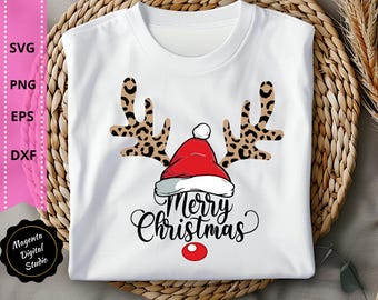 May include: White t-shirt featuring a Christmas reindeer design. The design includes leopard print antlers, a red Santa hat, and the words "Merry Christmas" in a script font. A red dot serves as the reindeer's nose.