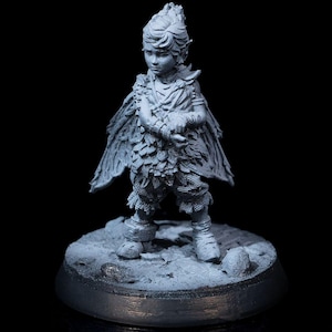 May include: A grey painted miniature figurine of a young person with wings, wearing a tunic and trousers, standing on a round base.