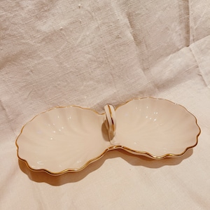 Może przedstawiać: Biała ceramiczna tacka do serwowania z pozłacanym rantem i uchwytem. Taca jest podzielona na dwie sekcje.