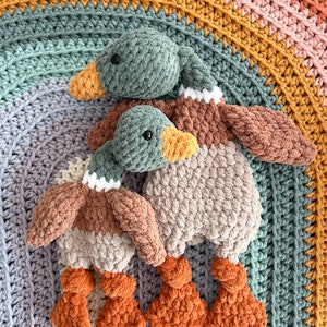 May include: Two crocheted duck plushies, one green and one brown, with orange feet. The ducks are sitting on a multi-colored crocheted blanket.