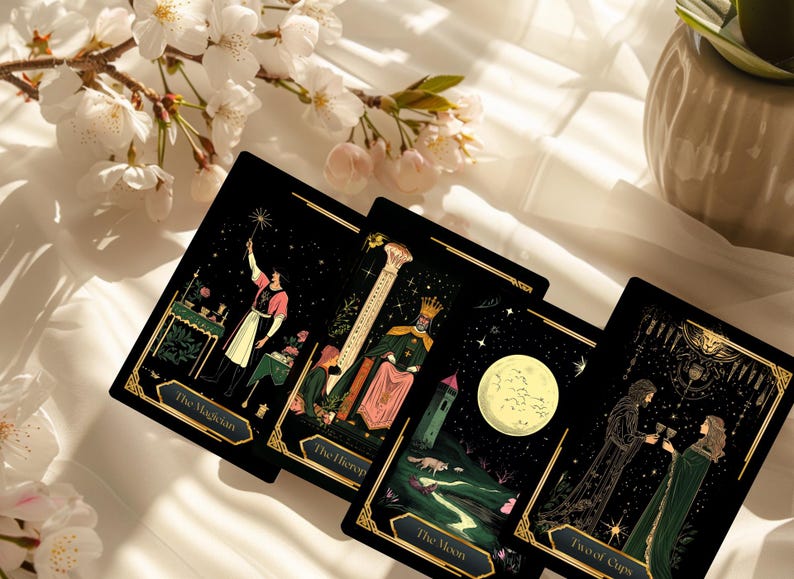 May include: Four tarot cards with black backgrounds and gold borders are displayed. The cards feature illustrations of The Magician, The Hierophant, The Moon, and Two of Cups. White flowers and a vase are in the background.