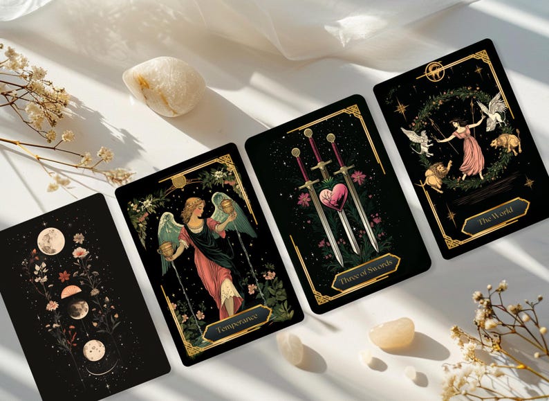 May include: Four tarot cards with black backgrounds and gold borders are displayed. The cards feature illustrations of angels, swords, and celestial bodies. Decorative elements include flowers and moons. Two small, light-colored stones and dried flowers are also present.
