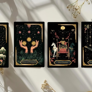 May include: Four tarot cards with black backgrounds and gold accents. The cards feature illustrations of the Ace of Wands, Three of Pentacles, The Chariot, and The Hanged Man. Each card has a unique design with celestial and mystical elements.