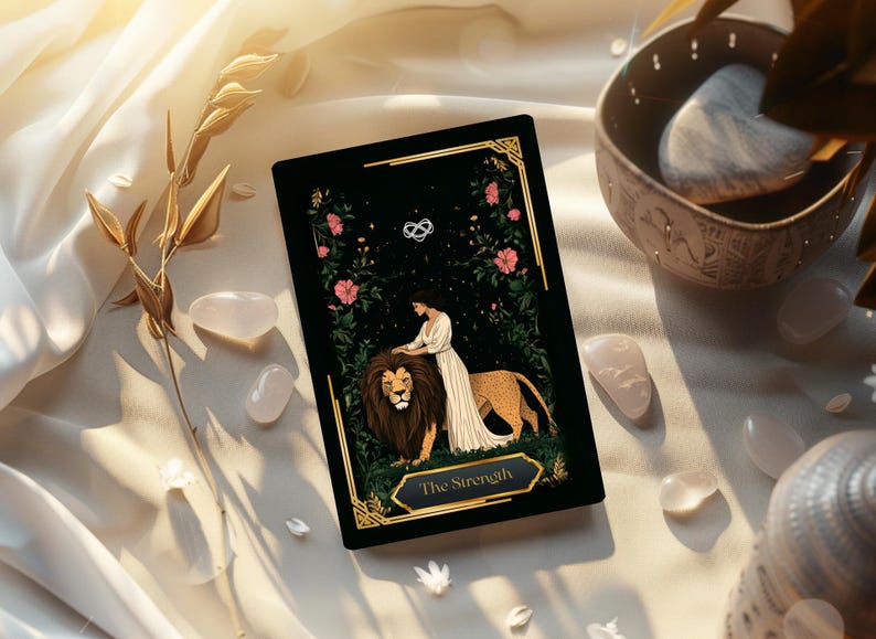 May include: A tarot card with a black background featuring a woman and a lion, labeled "The Strength." Pink flowers and gold accents frame the image. The card rests on a white cloth with quartz crystals and a decorative bowl.