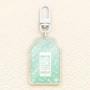 May include: A clear acrylic keychain with a white clasp and a mint green design. The keychain features a repeating key pattern and the French text "CONTRE LES CLÉS QUI PENSENT QUE TA PANIQUE MATINALE EST UNE BLAQUE DRÔLE".