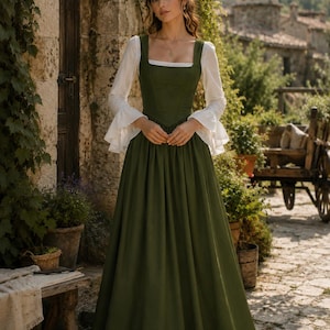 May include: A floor-length olive green dress featuring a square neckline and a fitted bodice. The dress is layered over a white long-sleeved blouse with flared, ruffled cuffs. The skirt is full and pleated at the waist, creating a structured silhouette.