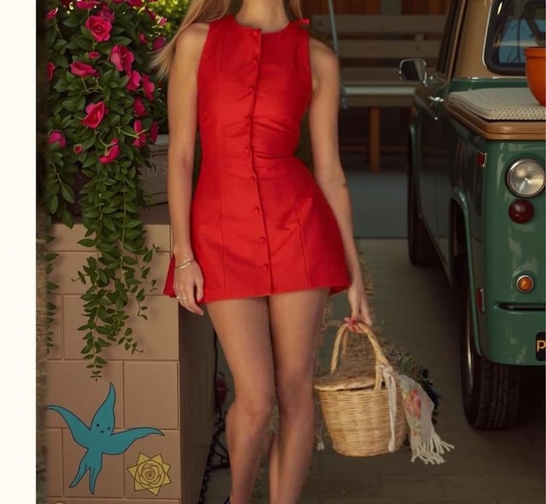 Pu&ograve; includere: Un vestito rosso senza maniche con bottoni. L'abito &egrave; abbinato a un cestino di vimini. Lo sfondo include un veicolo vintage verde e una composizione floreale. L'abito &egrave; in stile mini.