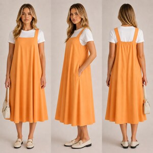 May include: An orange midi-length overall dress worn over a white t-shirt. The dress has wide shoulder straps and pockets. The model is wearing white loafers and carrying a white handbag. The dress is made of a soft, flowing fabric.