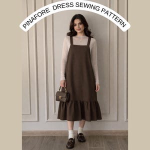 May include: A woman wearing a brown pinafore dress with a ruffled hem, paired with a long-sleeved top, white socks, and loafers. The dress has a square neckline and shoulder straps. The text "PINAFORE DRESS SEWING PATTERN" is arched above the woman.