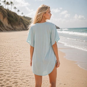 Puede incluir: Una t&uacute;nica playera azul claro con mangas cortas y dobladillo redondeado. La t&uacute;nica se usa en una playa de arena con el oc&eacute;ano al fondo. La modelo est&aacute; de espaldas a la c&aacute;mara.