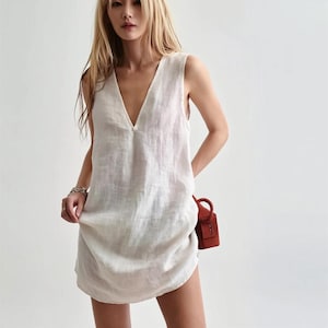 May include: A white sleeveless linen dress with a deep V-neckline. The dress has a relaxed fit and a slightly rounded hemline.