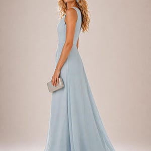 以下が含まれることがあります： 淡いブルーのノースリーブのイブニングドレス。流れるようなスカートが特徴です。フィットしたボディスと、控えめなウエストのディテールがあります。シルバーのクラッチバッグが持たれています。モデルはシルバーのサンダルとイヤリングを着用しています。