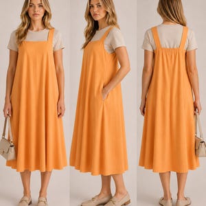 May include: An orange midi dress with wide shoulder straps and a square neckline, worn over a light-coloured t-shirt. The model wears beige loafers and carries a beige handbag. The dress has a relaxed fit and a flared skirt. The dress is approximately 100 cm in length.