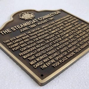 Puede incluir: Una placa hist&oacute;rica de metal color bronce oscuro con letras doradas en relieve y un emblema de barco de vapor. El texto dice: THE STEAMBOAT CONNECTION, JUNE, 1888 - AUGUST, 1941, seguido de una descripci&oacute;n hist&oacute;rica detallada del lugar.