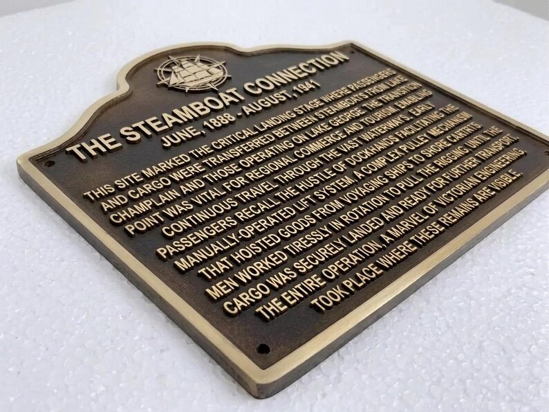 Puede incluir: Una placa hist&oacute;rica de metal color bronce oscuro con letras doradas en relieve y un emblema de barco de vapor. El texto dice: THE STEAMBOAT CONNECTION, JUNE, 1888 - AUGUST, 1941, seguido de una descripci&oacute;n hist&oacute;rica detallada del lugar.