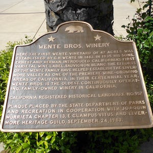 Puede incluir: Una placa hist&oacute;rica de metal color bronce titulada Wente Bros. Winery. La placa presenta un emblema de oso, dos estrellas y texto en relieve que detalla la historia del vi&ntilde;edo establecido en 1883, designado como California Landmark No. 957.
