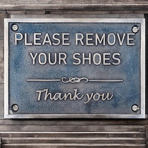 May include: A blue metal sign with the text "PLEASE REMOVE YOUR SHOES Thank you" in silver lettering.