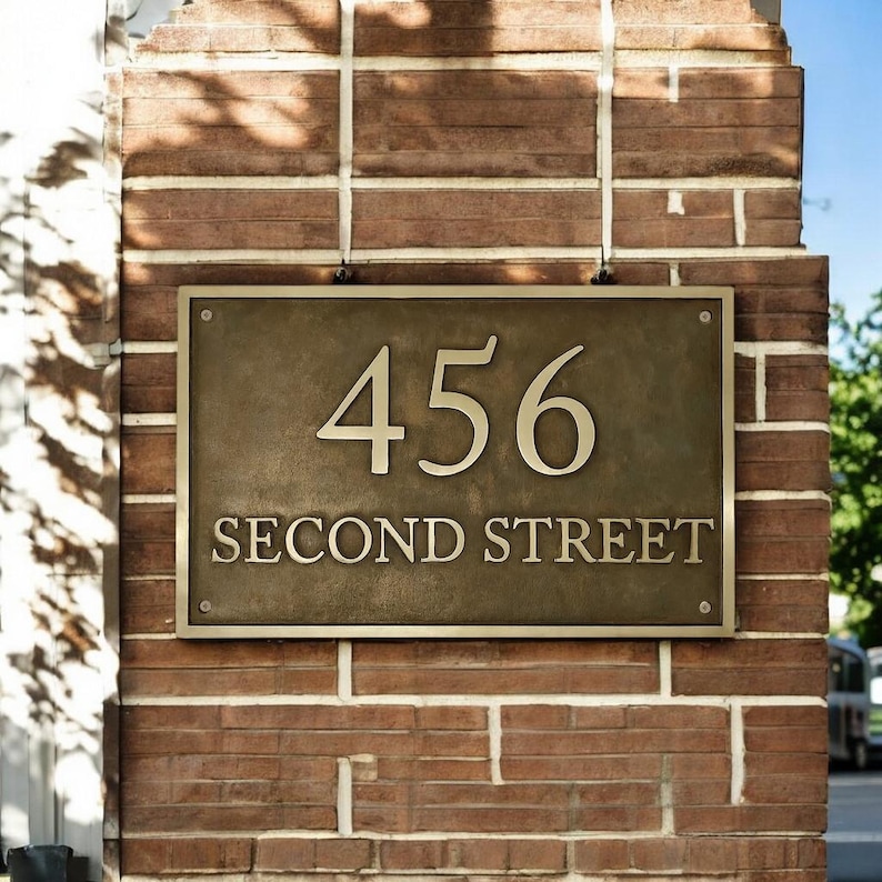 May include: A rectangular bronze-colored metal plaque mounted on a brick wall. The plaque features the number 456 in large, raised numerals above the text SECOND STREET in smaller, raised capital letters, secured by four visible corner screws.