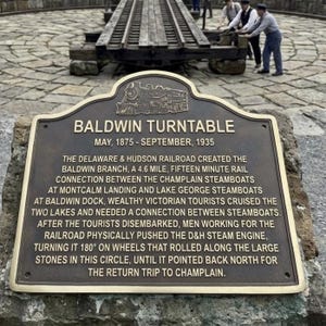 Puede incluir: Una placa hist&oacute;rica de metal color bronce titulada Baldwin Turntable, mayo de 1875 - septiembre de 1935. La placa presenta un relieve de una locomotora de vapor y un texto detallado que explica la historia de la conexi&oacute;n ferroviaria Delaware & Hudson.