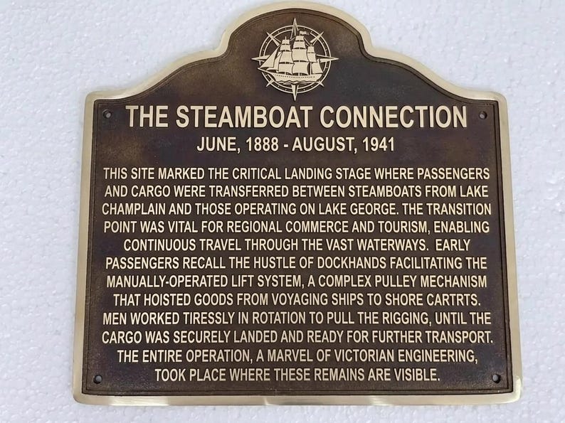 Puede incluir: Una placa rectangular de bronce con la parte superior redondeada que presenta un emblema en relieve de un barco de vapor y una br&uacute;jula. El texto dice THE STEAMBOAT CONNECTION, JUNE, 1888 - AUGUST, 1941, seguido de una descripci&oacute;n hist&oacute;rica.