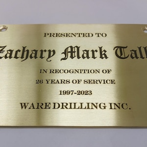 May include: A rectangular brass plaque with rounded corners and four mounting holes. The plaque features engraved text: "PRESENTED TO Zachary Mark Tally IN RECOGNITION OF 26 YEARS OF SERVICE 1997-2023 WARE DRILLING INC."