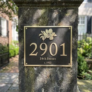 May include: A rectangular dark bronze house plaque featuring a raised gold floral emblem at the top, the number 2901 in large gold numerals, and the text 34th Street and c. 1922 in smaller gold lettering, secured with four gold corner screws.