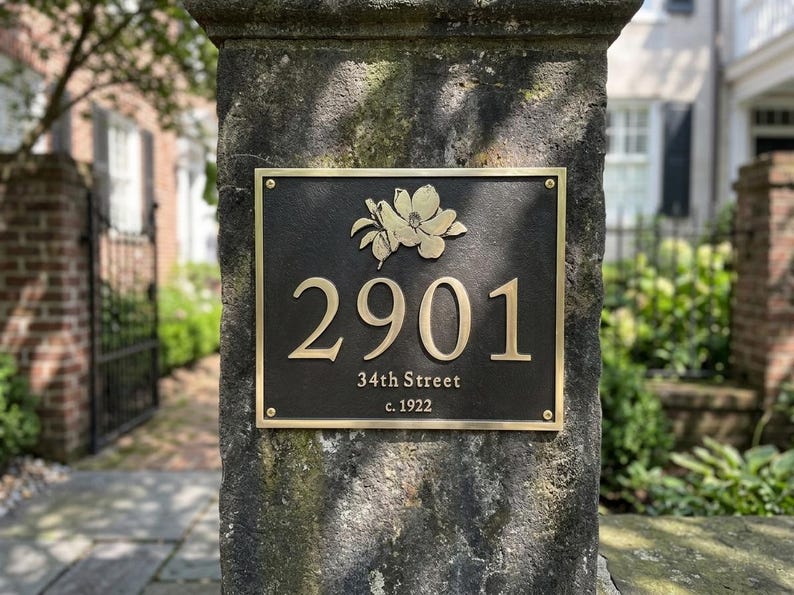 May include: A rectangular dark bronze house plaque featuring a raised gold floral emblem at the top, the number 2901 in large gold numerals, and the text 34th Street and c. 1922 in smaller gold lettering, secured with four gold corner screws.