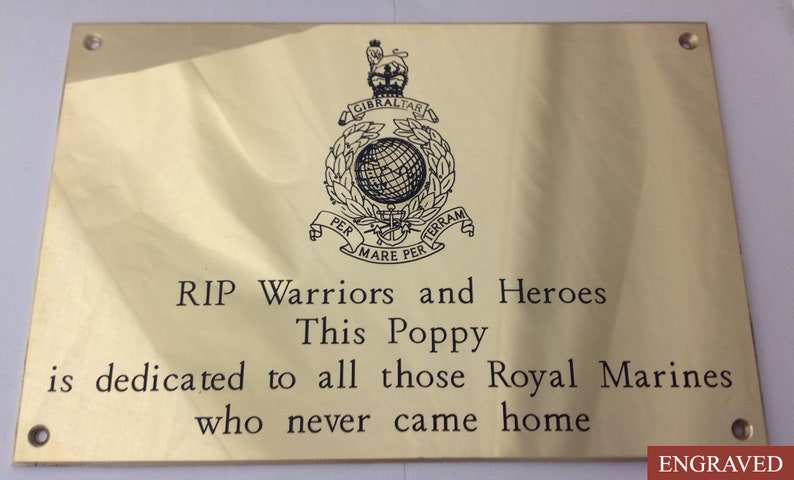 May include: A rectangular, gold-colored plaque with engraved text and a crest. The text reads "RIP Warriors and Heroes" and "This Poppy is dedicated to all those Royal Marines who never came home." The crest includes a globe and the words "Gibraltar" and "Per Mare Per Terram."
