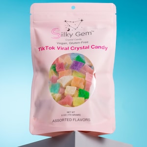 May include: A pink bag of "Silky Gem" crystal candy. The bag has a clear window showing colorful, assorted flavors of the vegan and gluten-free candy. The bag is labeled "TikTok Viral Crystal Candy" and contains 6 oz (170 grams) of candy.
