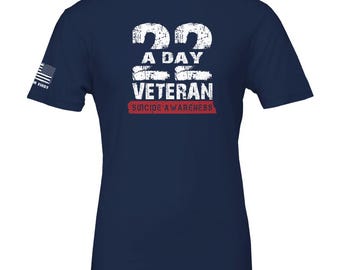 Op de afbeelding: Marineblauw T-shirt met de tekst "22 A DAY VETERAN SUICIDE AWARENESS" in verweerde witte letters. De Amerikaanse vlag staat op de linkermouw. Een T-shirt met ronde hals en korte mouwen.