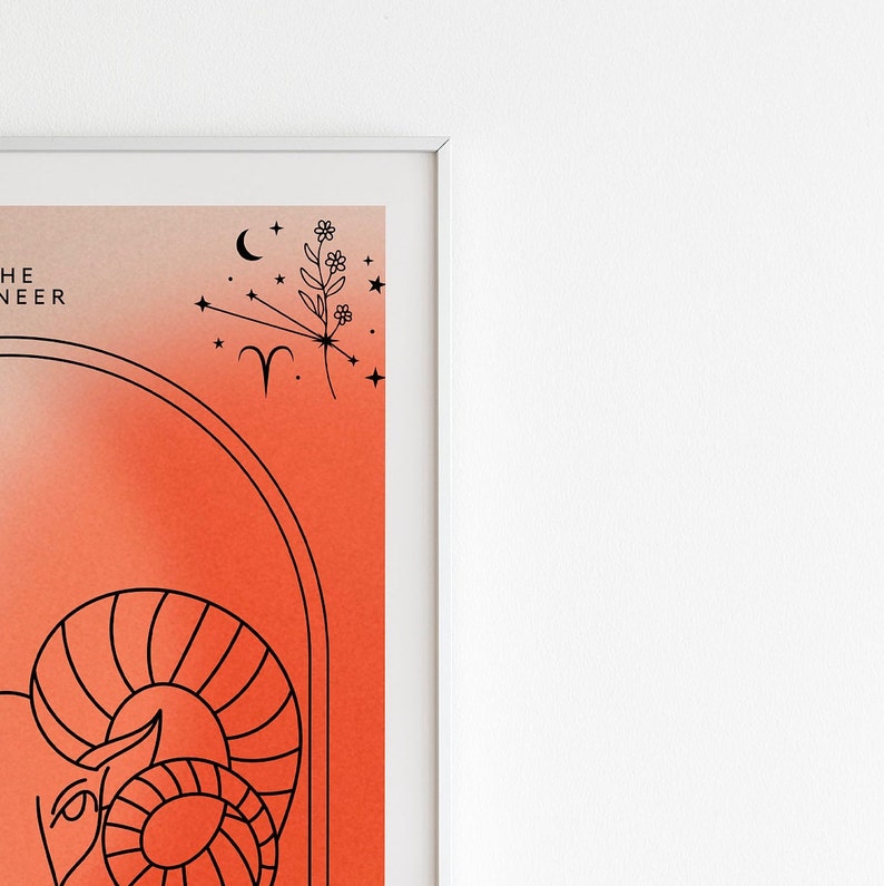 May include: A white framed print with a red and orange gradient background. The print features a black line drawing of an astrological ram symbol with stars and a flower. The text "THE RAM" is at the top of the print.
