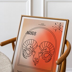 May include: A framed print with a red and orange gradient background featuring a line drawing of an Aries zodiac sign. The text "Aries" is in black lettering and the text "The Pioneer" is in black lettering. The text "Fire sign n.01" and "Cardinal" are also in black lettering.