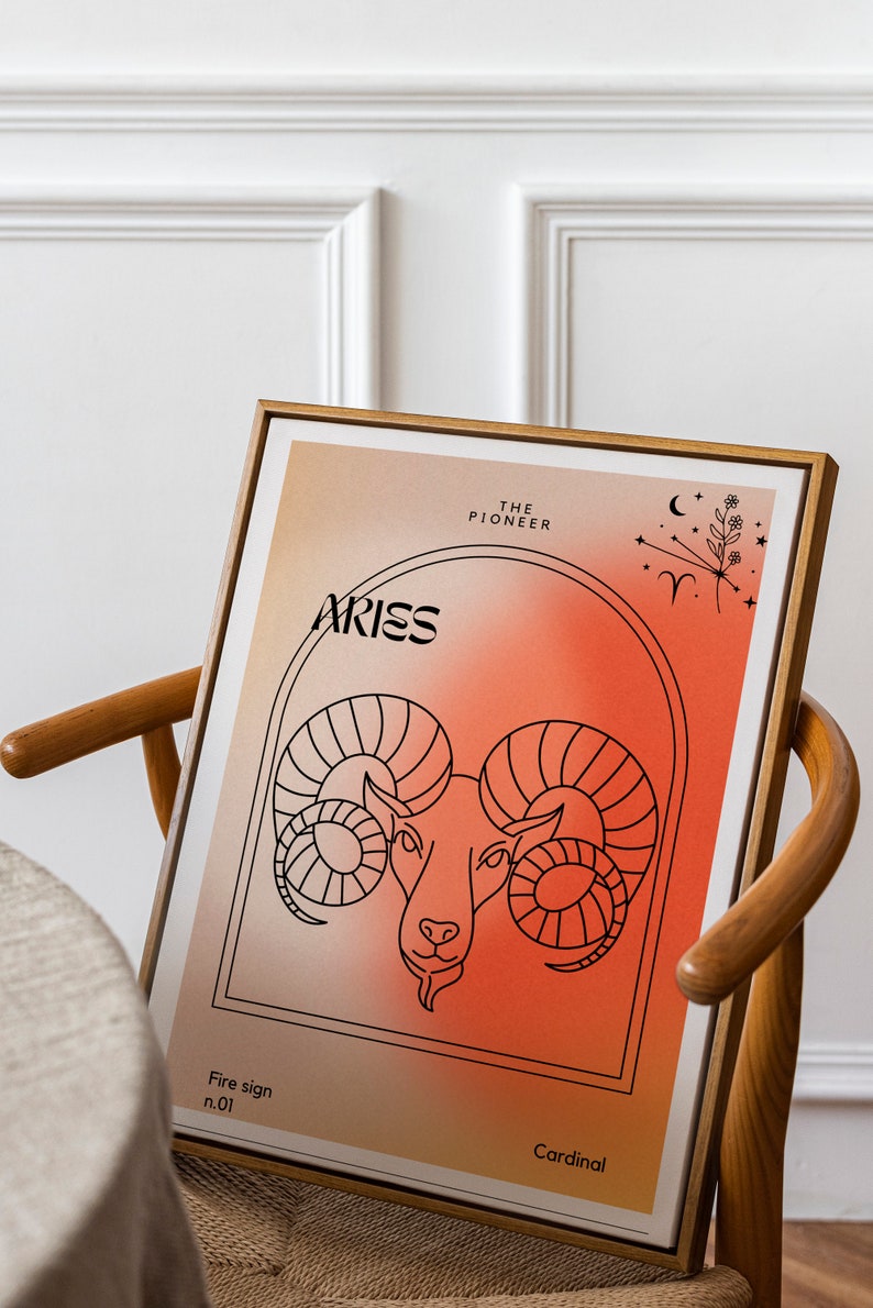May include: A framed print with a red and orange gradient background featuring a line drawing of an Aries zodiac sign. The text "Aries" is in black lettering and the text "The Pioneer" is in black lettering. The text "Fire sign n.01" and "Cardinal" are also in black lettering.