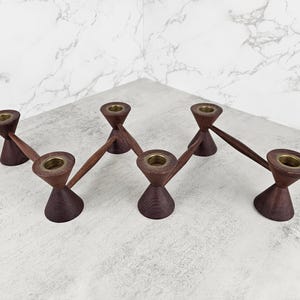 May include: A mid-century modern candle holder with six candle cups. The candle holder is made of dark brown wood with brass-colored candle cups. The design features a geometric, angular shape, suitable for a dining table or mantelpiece.