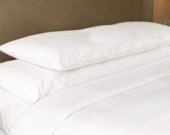 May include: A set of crisp white bed linens consisting of a flat sheet, a fitted sheet, and two rectangular pillows stacked neatly on top of each other. The bedding is smooth and clean, featuring a plain, solid white color throughout the set.