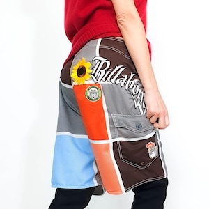 Op de afbeelding: Meerkleurige zwembroek met een Billabong-logo en een zonnebloemdessin. De zwembroek heeft een bruin, grijs, oranje, blauw en roze kleurenschema.