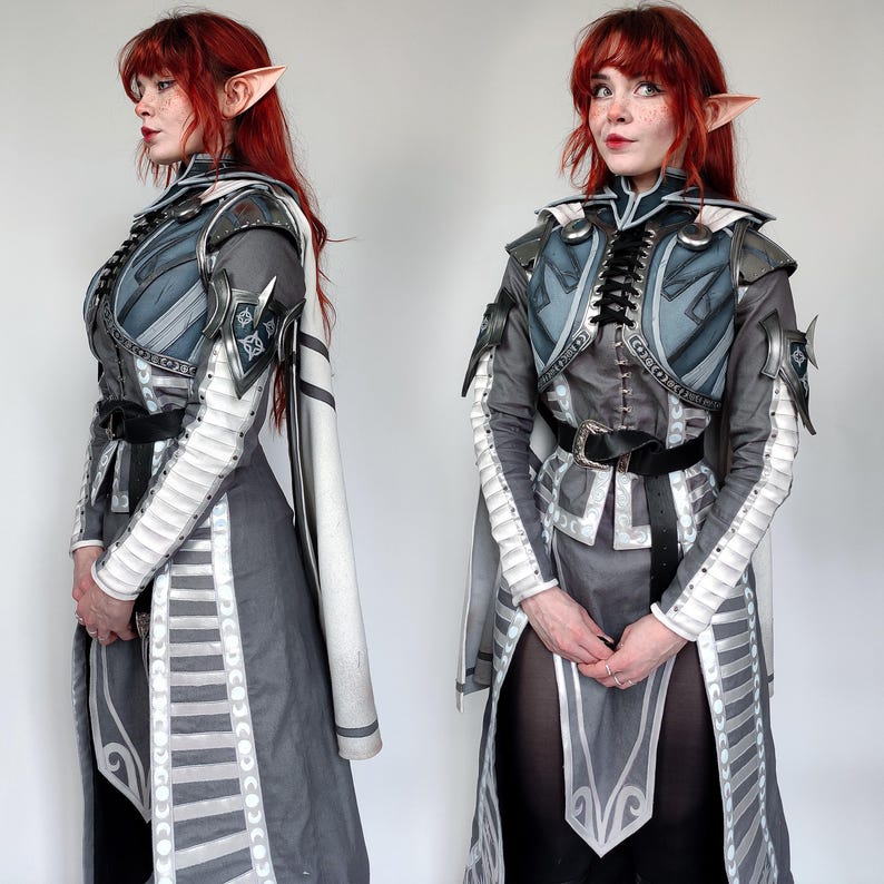 May include: A woman in a grey and white costume with a silver breastplate and matching gauntlets. She has red hair and pointed ears.