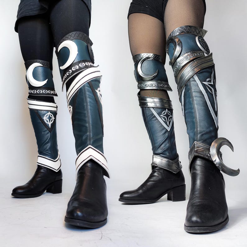 May include: A pair of black leather boots with silver accents and blue fabric knee-high coverings. The coverings have a crescent moon design and white accents.