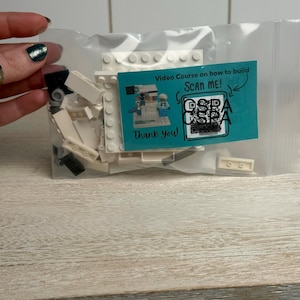 May include: A clear plastic bag containing white and black building blocks and a teal card. The card reads "Video Course on how to build SCAN ME!" with a QR code and the words "Thank you!"