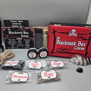 May include: A collection of items for a themed box set, including a red box with a skull and crossbones, a black candle, and small packets labeled "Charcoal," "Sage," and "Wormwood." The box is labeled "The Blackened Box Curse."