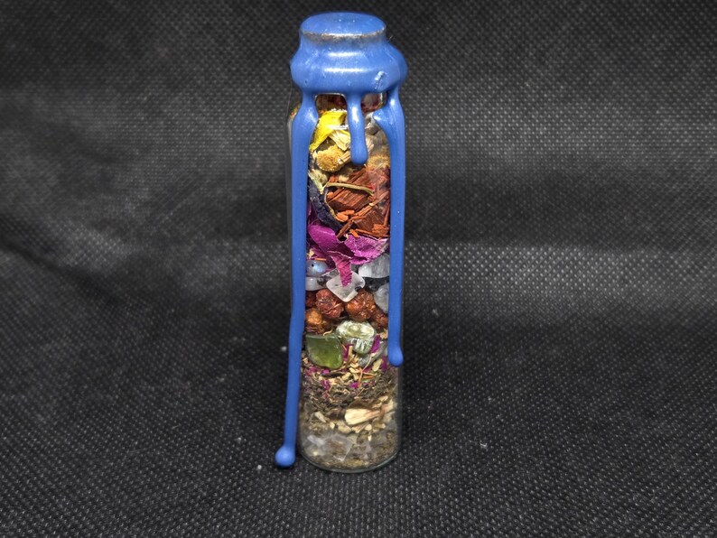 K&ouml;nnte beinhalten: Eine kleine Glasflasche gef&uuml;llt mit getrockneten Kr&auml;utern, Samen und Kristallen. Die Flasche ist mit blauem Wachs versiegelt, das an den Seiten herunterl&auml;uft. Durch das klare Glas sind die Inhalte mit verschiedenen Farben und Texturen sichtbar.