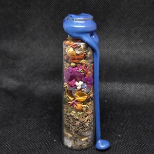 K&ouml;nnte beinhalten: Eine klare Glasflasche gef&uuml;llt mit getrockneten Kr&auml;utern, Blumen und Kristallen. Die Flasche ist mit blauem Wachs versiegelt, das an der Seite heruntertropft. Der Inhalt der Flasche ist eine Mischung aus Farben, darunter Lila, Gold und Gr&uuml;n.