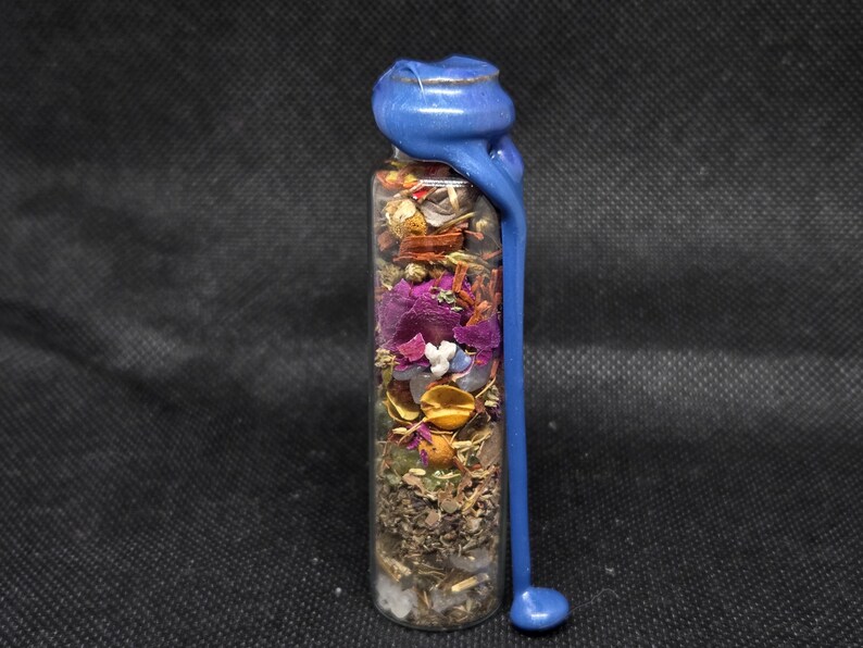 K&ouml;nnte beinhalten: Eine klare Glasflasche gef&uuml;llt mit getrockneten Kr&auml;utern, Blumen und Kristallen. Die Flasche ist mit blauem Wachs versiegelt, das an der Seite heruntertropft. Der Inhalt der Flasche ist eine Mischung aus Farben, darunter Lila, Gold und Gr&uuml;n.