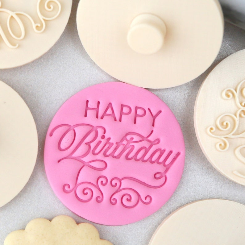 May include: Pink silicone stamp with the text "Happy Birthday" in a cursive font. The stamp is surrounded by a decorative border of swirls.