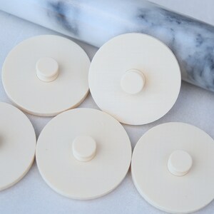 May include: Five off-white round silicone jar lids with a small round knob in the center of each lid.