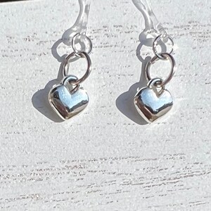 May include: A pair of silver heart charm earrings with clear plastic earring backs.