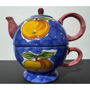 Puede incluir: Juego de té de cerámica azul con motivos de manzanas amarillas y hojas verdes. El juego incluye una tetera y una taza apilables. Las asas y el pico son de color burdeos. Un juego de vajilla decorativo y colorido.
